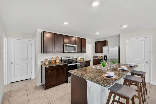 a kitchen with stainless steel appliances kitchen island granite countertop a stove a sink a refrigerator a dining table and chairs with wooden floor