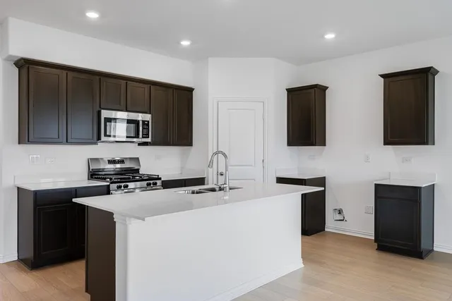 a kitchen with stainless steel appliances a sink a stove a microwave a refrigerator a sink and cabinets