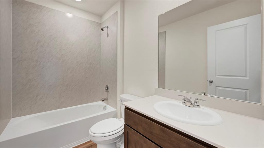 4012 Ripplewood Drive Lindale, TX 75771 - Photo 2 of 37 Bathroom featuring a white vanity with an undermount sink, a large mirror, a chrome faucet, a white toilet, and a bathtub with a light-toned shower surround