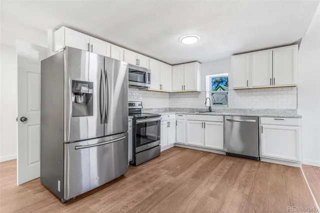 a kitchen with white cabinets stainless steel appliances and wooden floor