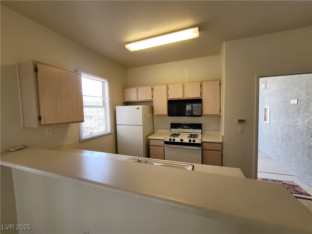 7413 West Russell Road, Unit 107 Las Vegas, NV 89113 - Photo 17 of 48 Kitchen with white appliances, light brown cabinetry, a sink, light countertops, and a peninsula