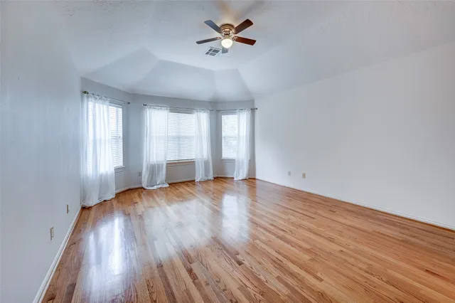 an empty room with wooden floor chandelier fan and windows