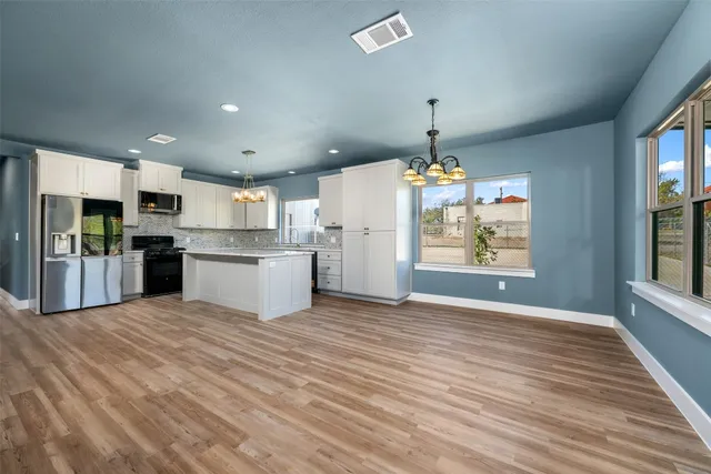 a large kitchen with stainless steel appliances kitchen island granite countertop a stove a sink dishwasher and a refrigerator with wooden floor