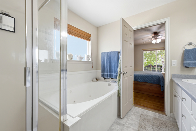 5196 Rodeo Circle Oakley, UT 84055 - Photo 24 of 57 Primary suite bathroom with a glass-enclosed shower, built-in soaking tub, a window with a wood-slat blind, and a vanity with a countertop and under-sink cabinetry