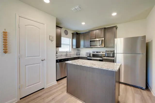 a kitchen with stainless steel appliances granite countertop a refrigerator a stove a sink a microwave and white cabinets with wooden floor