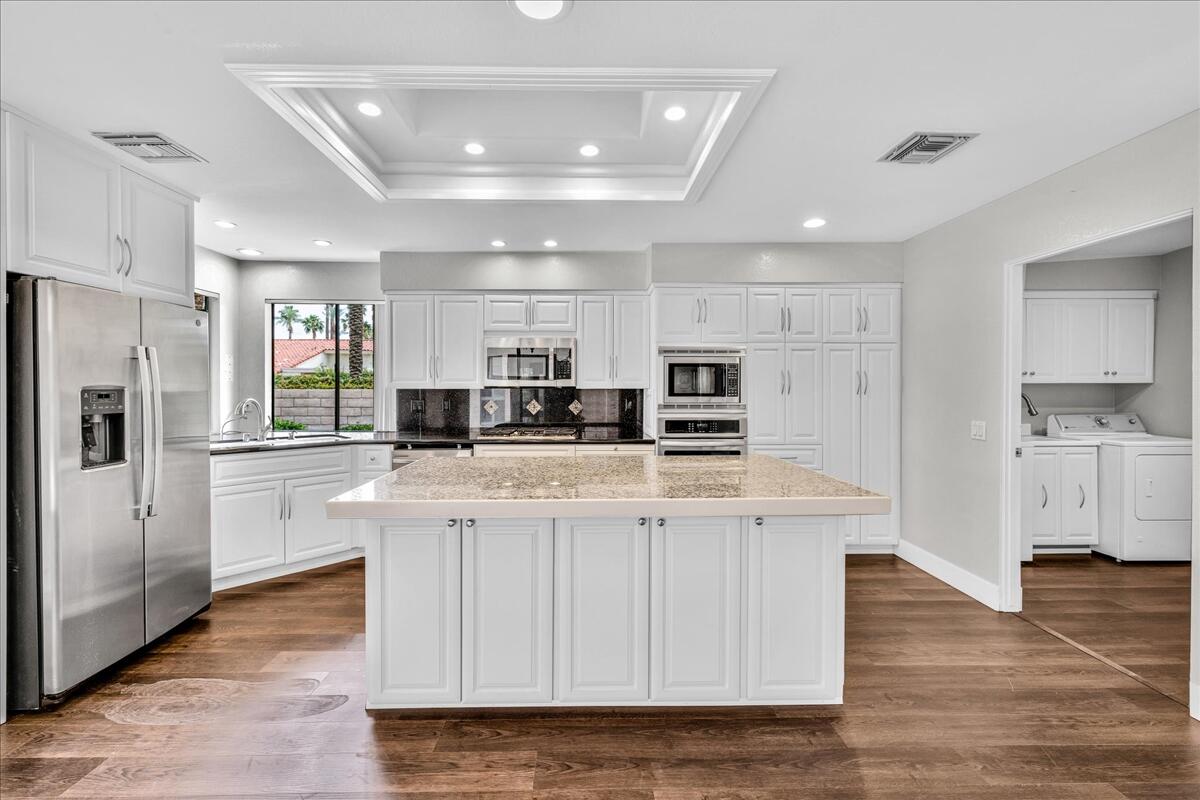 45 Lincoln Place Rancho Mirage, CA 92270 - Photo 8 of 59 a kitchen with stainless steel appliances kitchen island granite countertop a refrigerator a stove a sink dishwasher and white cabinets with wooden floor