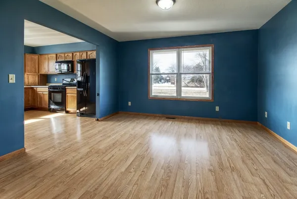 an empty room with wooden floor and a kitchen