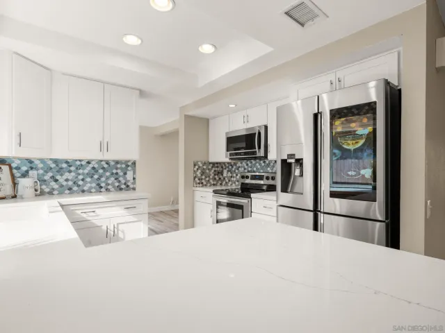 a large kitchen with kitchen island a stove a sink dishwasher a refrigerator oven with white cabinets and wooden floor