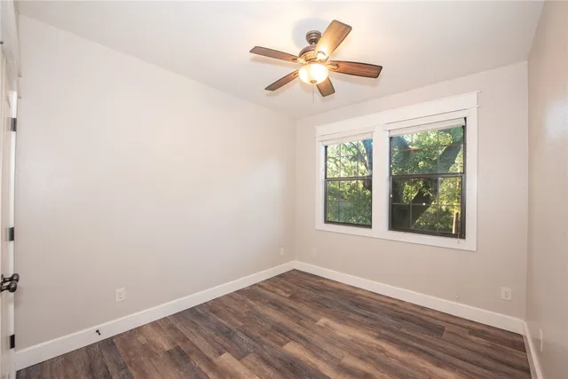 an empty room with wooden floor fan and windows