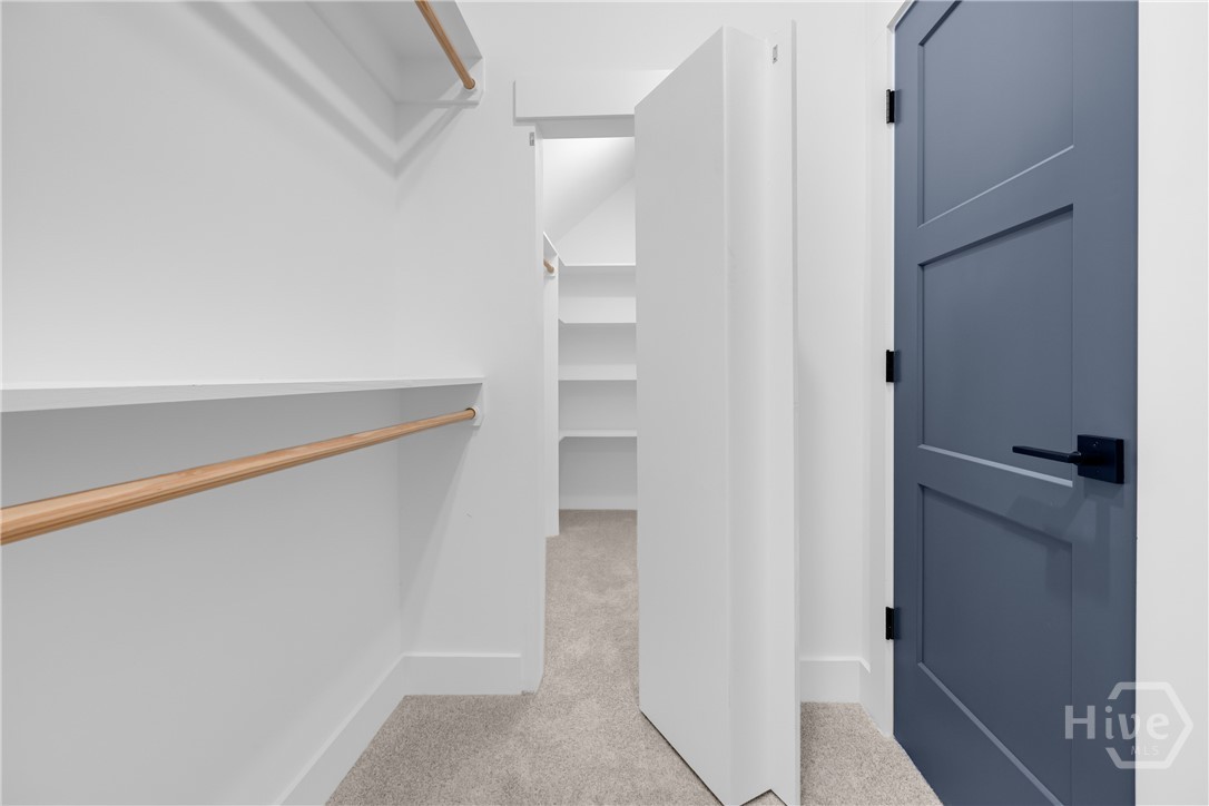 2476 St Martin Way Monroe, GA 30656 - Photo 48 of 75 Secret Passageway in Walk-in closet featuring light-colored carpeting, multiple shelving units, and two wooden hanging rods