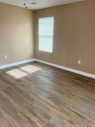 a view of an empty room with wooden floor and a window