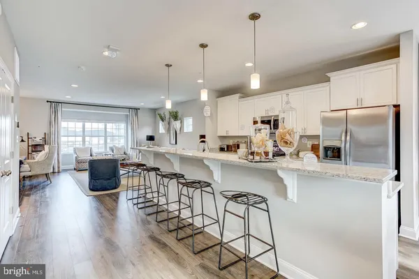 a kitchen with stainless steel appliances kitchen island granite countertop a refrigerator a stove a sink a dining table and chairs with wooden floor