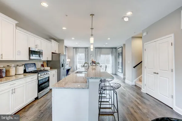 a kitchen with kitchen island granite countertop a stove a sink a refrigerator and white cabinets with wooden floor