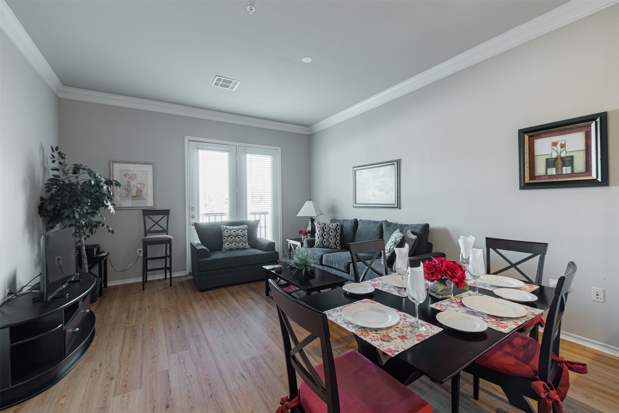 Bright and inviting living-dining area featuring sleek hardwood flooring, a cozy sofa, and a stylish dining set, complemented by elegant decor and natural light from large windows.