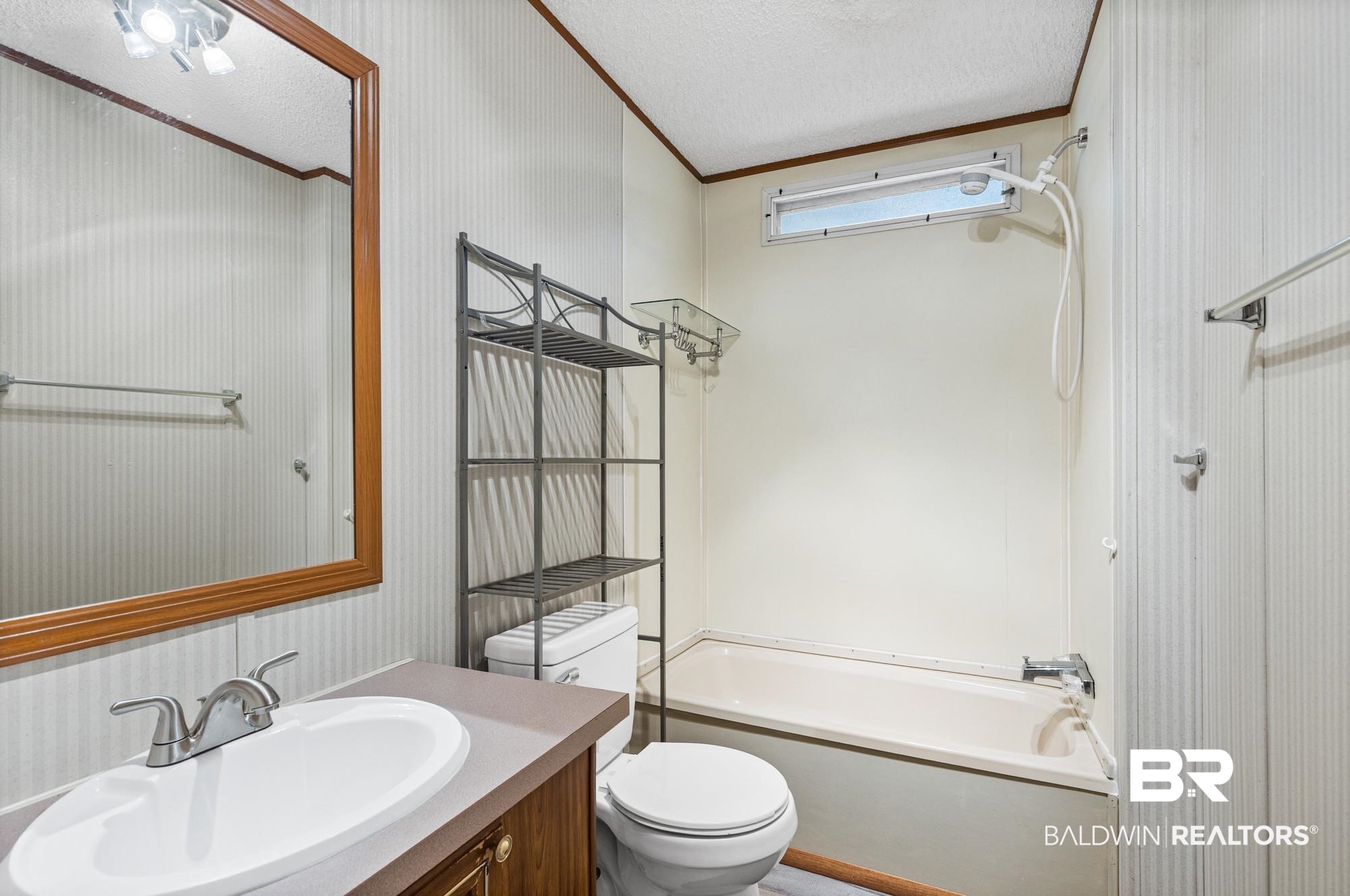 8675 Hunters Pointe Drive North Theodore, AL 36582 - Photo 16 of 20 Bathroom featuring a single vanity with a white oval sink, a wall-mounted mirror with wood-finish frame, a tub/shower combination with a horizontal window, and white vertical paneled walls