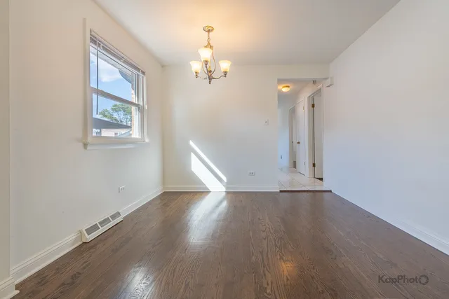 an empty room with wooden floor chandelier and windows
