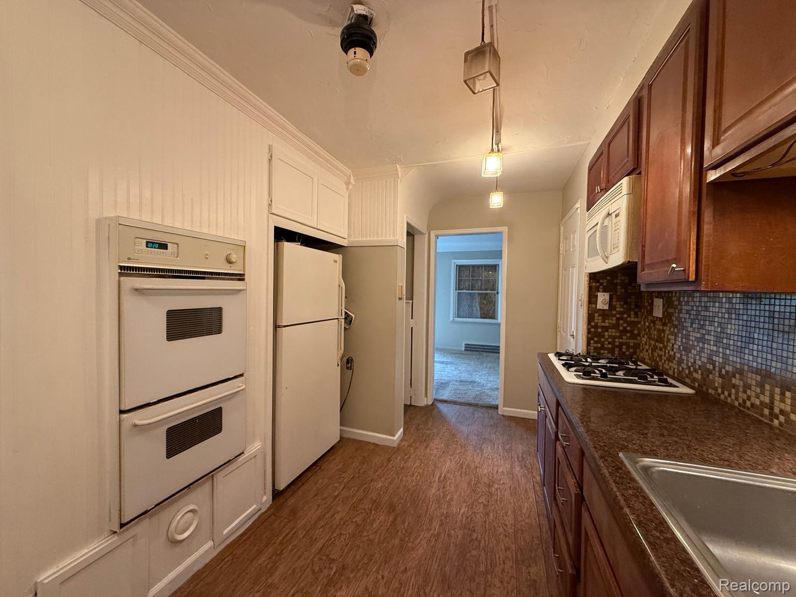 20231 Moross Road Detroit, MI 48224 - Photo 2 of 23 Kitchen with dark countertops, dark wood-type flooring, white appliances, backsplash, and decorative light fixtures