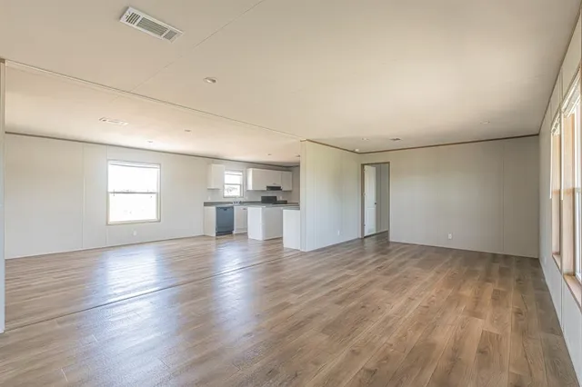 an empty room with wooden floor kitchen view and windows
