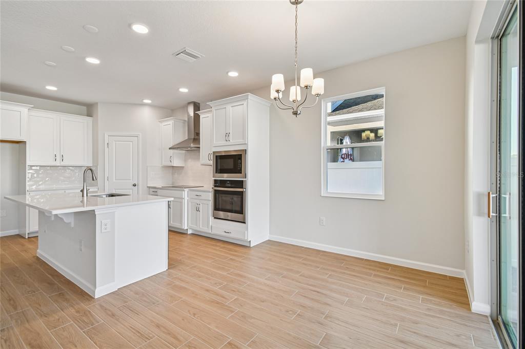 813 River Stone Trail Sanford, FL 32771 - Photo 4 of 33 a large white kitchen with kitchen island a stove a sink dishwasher and white cabinets with wooden floor