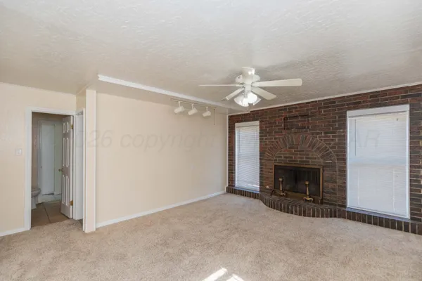 a view of an empty room with chandelier fan and fire place