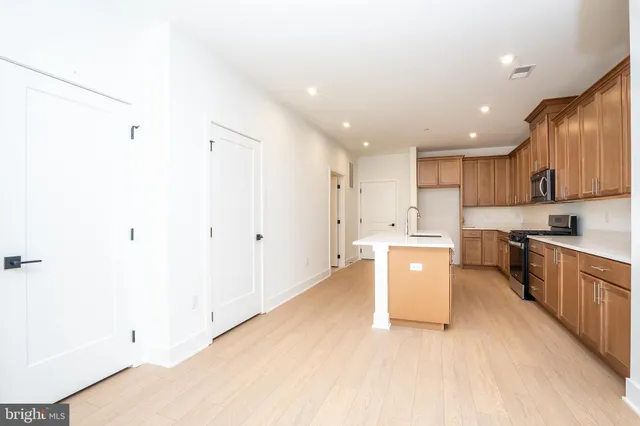 a large kitchen with a large counter top a sink stainless steel appliances and cabinets