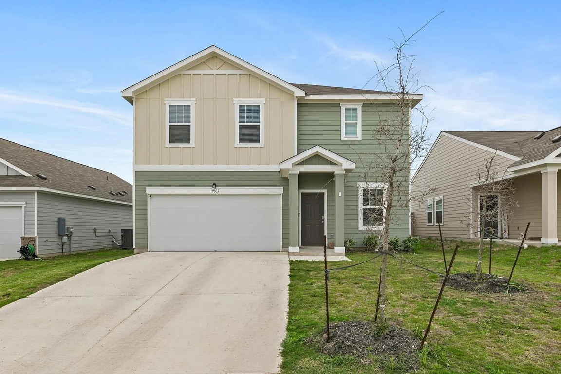 Traditional-style house featuring board and batten siding, concrete driveway, a front yard, and a garage