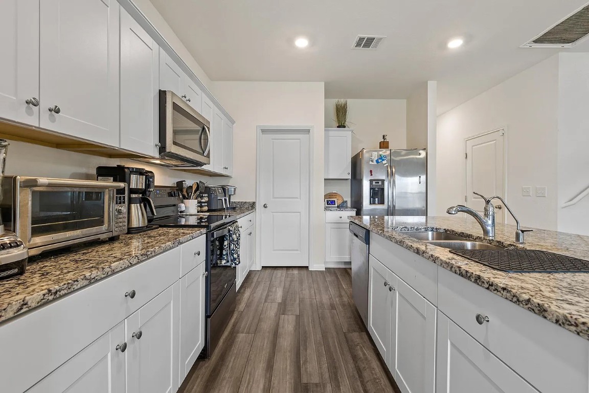 19605 Caymus Drive Pflugerville, TX 78660 - Photo 8 of 26 Kitchen featuring white cabinetry, appliances with stainless steel finishes, dark wood-style floors, light stone countertops, and recessed lighting