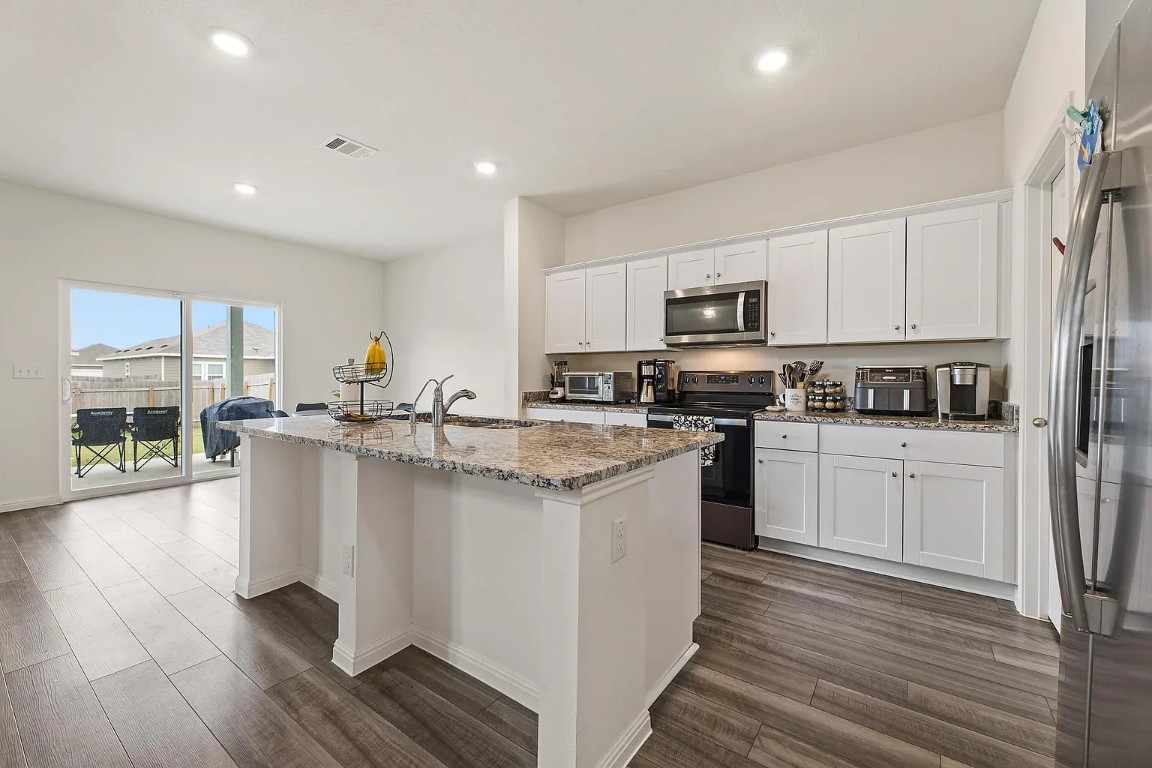 19605 Caymus Drive Pflugerville, TX 78660 - Photo 10 of 26 Kitchen featuring appliances with stainless steel finishes, white cabinets, light stone counters, recessed lighting, and a center island with sink