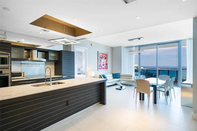 a dining hall with stainless steel appliances kitchen island granite countertop a table chairs and a refrigerator