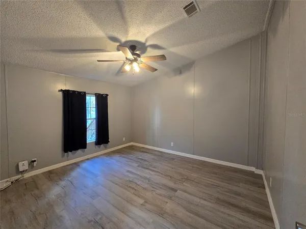 an empty room with wooden floor chandelier fan and windows
