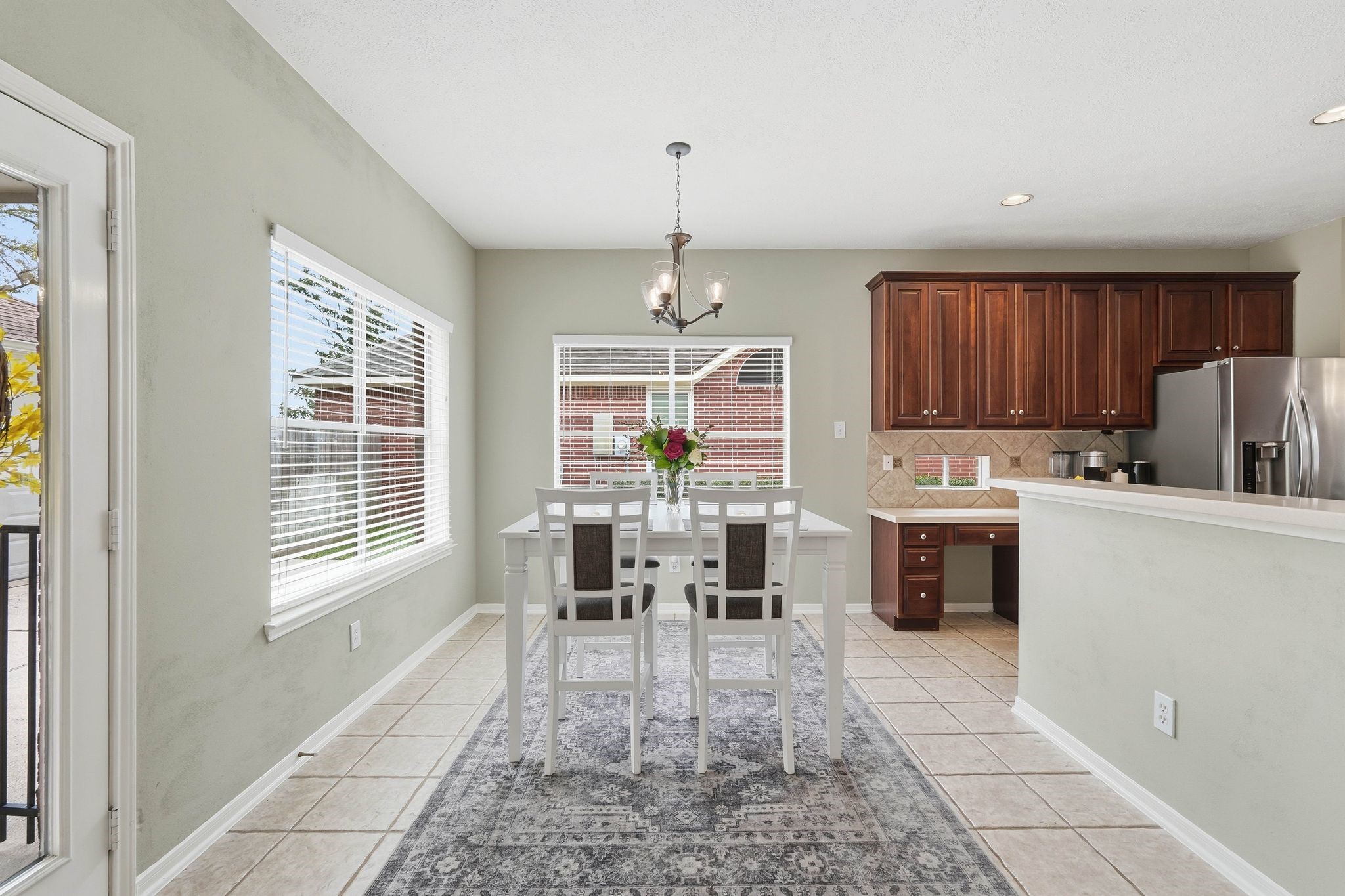2515 Woodsboro Drive Spring, TX 77388 - Photo 11 of 44 Bright dining area with large windows, a cozy table setting, and tile flooring. The kitchen features dark wood cabinets, stainless steel appliances, and a breakfast bar.