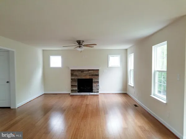 a view of an empty room with wooden floor fireplace and a window