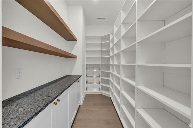 1620 Belayer Drive St. George, UT 84770 - Photo 26 of 51 Walk-in pantry featuring extensive white shelving, wood-finish floating shelves, a dark speckled countertop, white cabinetry with gold-tone hardware, and wood-finish flooring