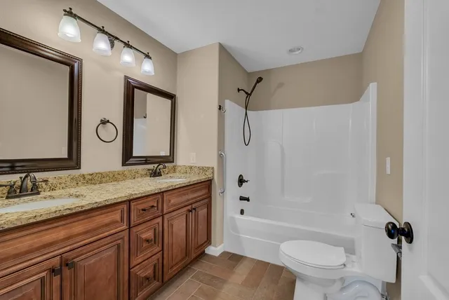 a bathroom with a granite countertop bathtub shower sink vanity mirror and toilet