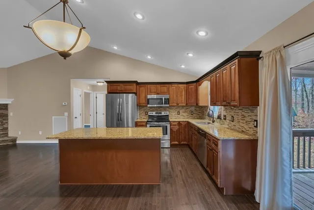 a large kitchen with stainless steel appliances granite countertop a large counter top a stove and a wooden floors