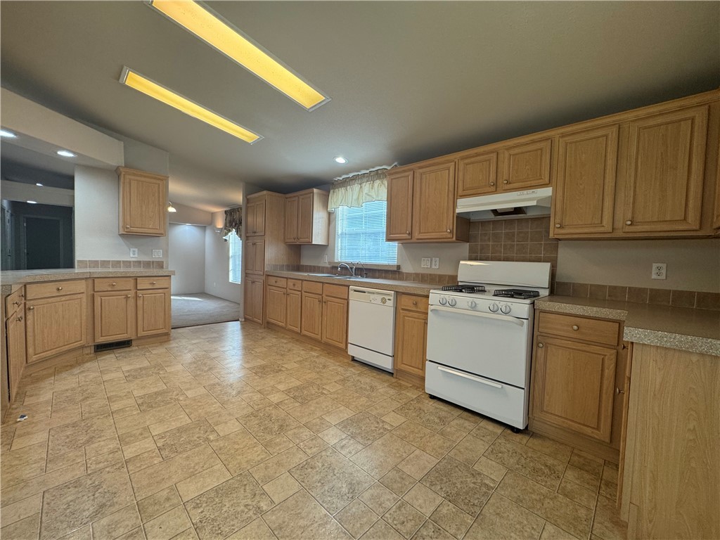 10044 Kent Road Mohave Valley, AZ 86440 - Photo 9 of 25 Kitchen featuring white appliances, light countertops, under cabinet range hood, light stone finish floors, and tasteful backsplash