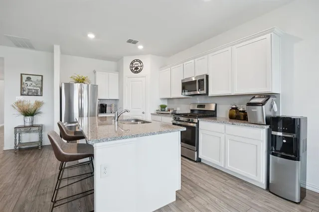 a kitchen with stainless steel appliances granite countertop a stove top oven a sink a refrigerator and white cabinets with wooden floor