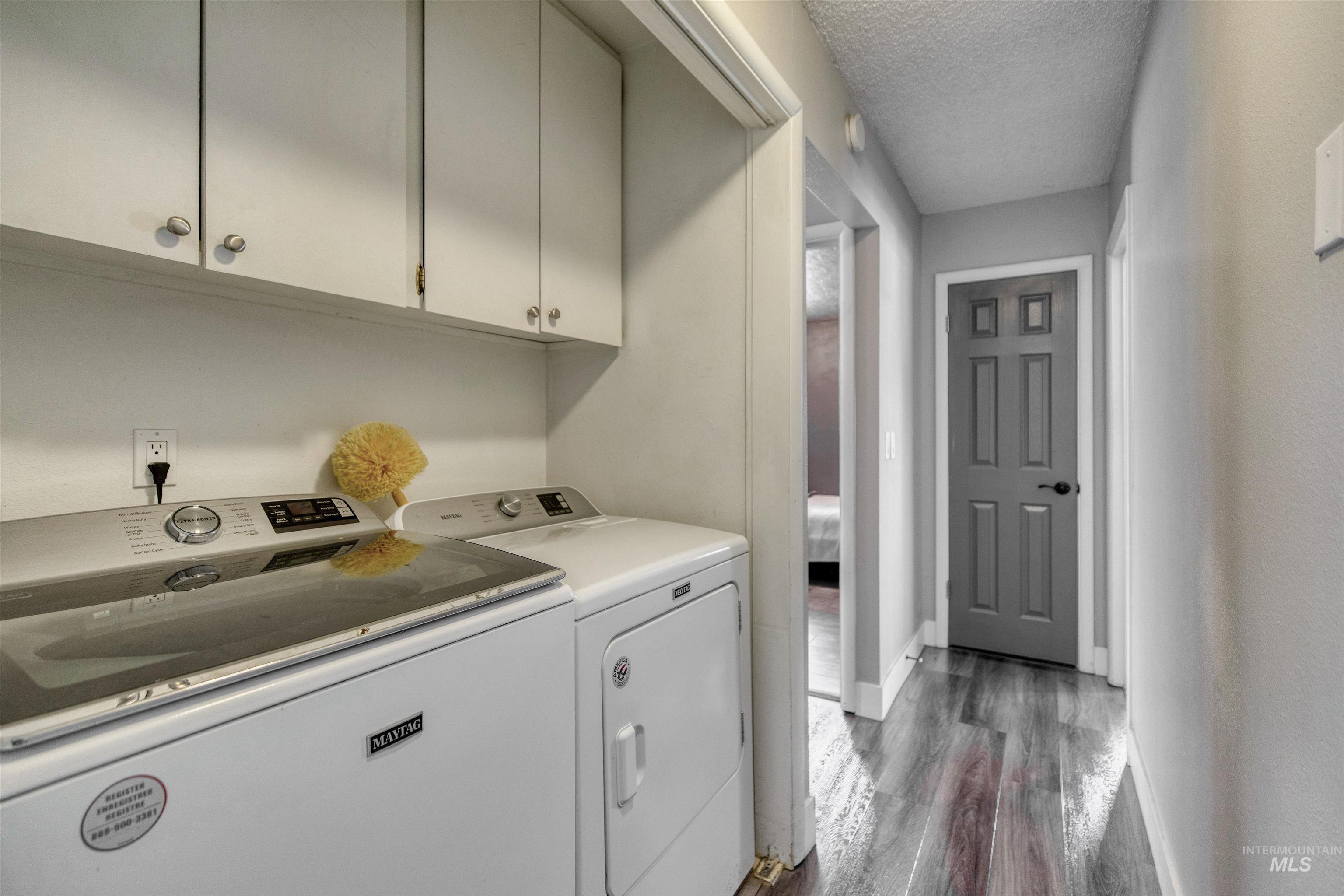 20803 Friends Road Greenleaf, ID 83626 - Photo 21 of 39 Dedicated laundry area featuring white upper cabinetry with brushed nickel hardware, and wood-finish flooring extending into a hallway with a gray paneled door