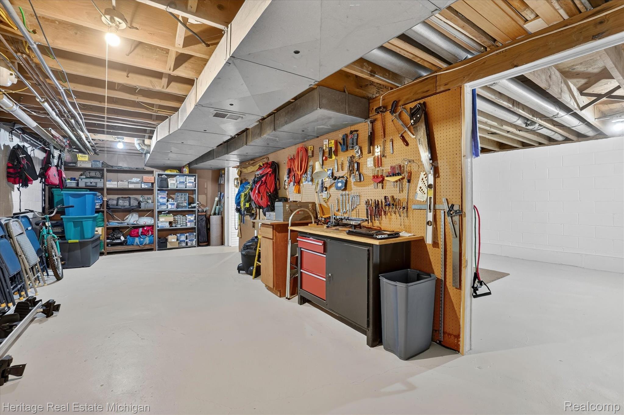 14038 North Hogan Road Linden, MI 48451 - Photo 40 of 53 Basement workshop area featuring a built-in workbench with storage cabinetry, pegboard wall, and exposed ceiling joists