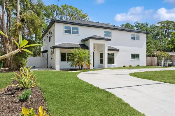 a view of a white house next to a yard with big trees