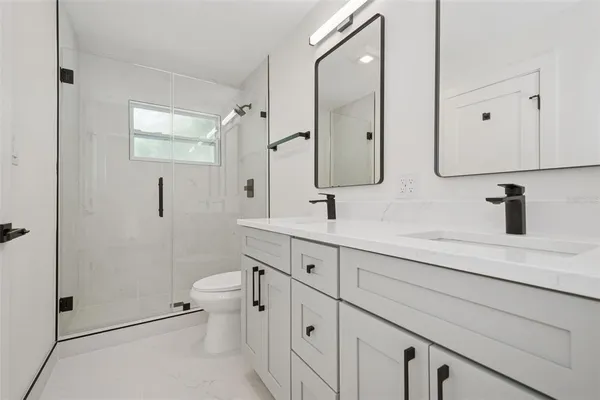 a spacious bathroom with double vanity sink a mirror a toilet and a shower