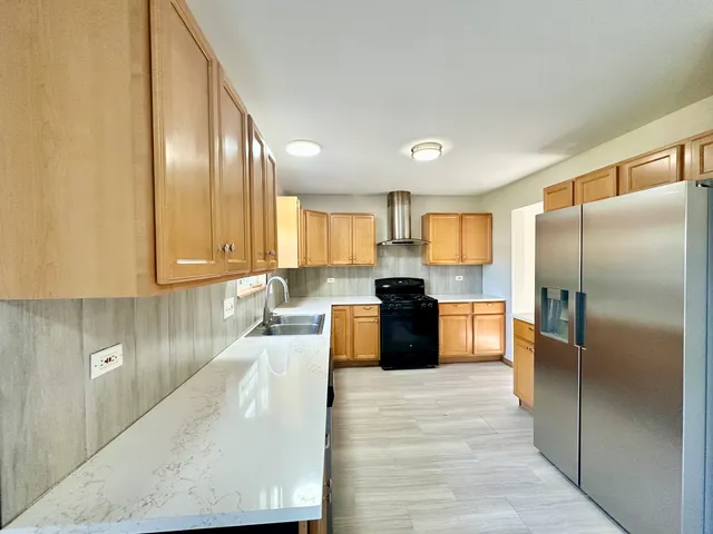 a large kitchen with granite countertop a large counter top stainless steel appliances a sink a refrigerator and cabinets