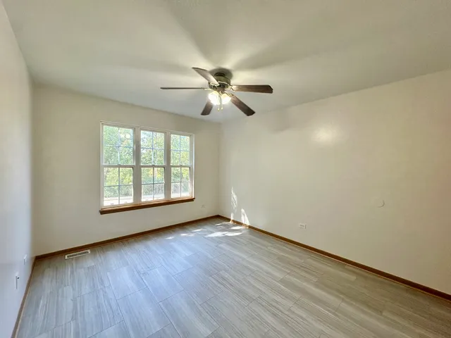 an empty room with wooden floor ceiling fan and windows