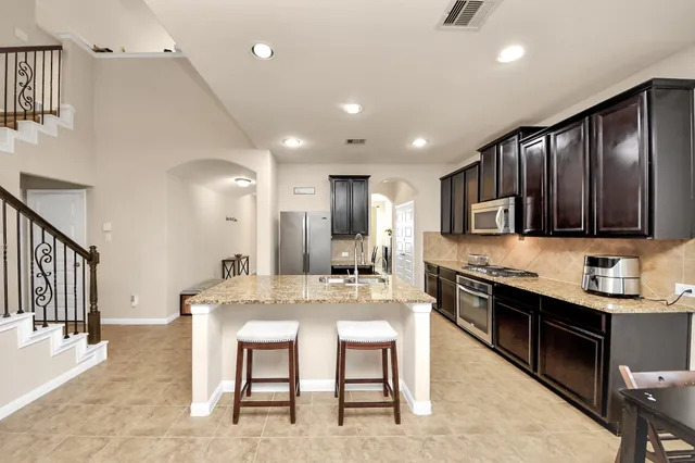 a kitchen with stainless steel appliances granite countertop a stove top oven a sink dishwasher a dining table and chairs with wooden floor