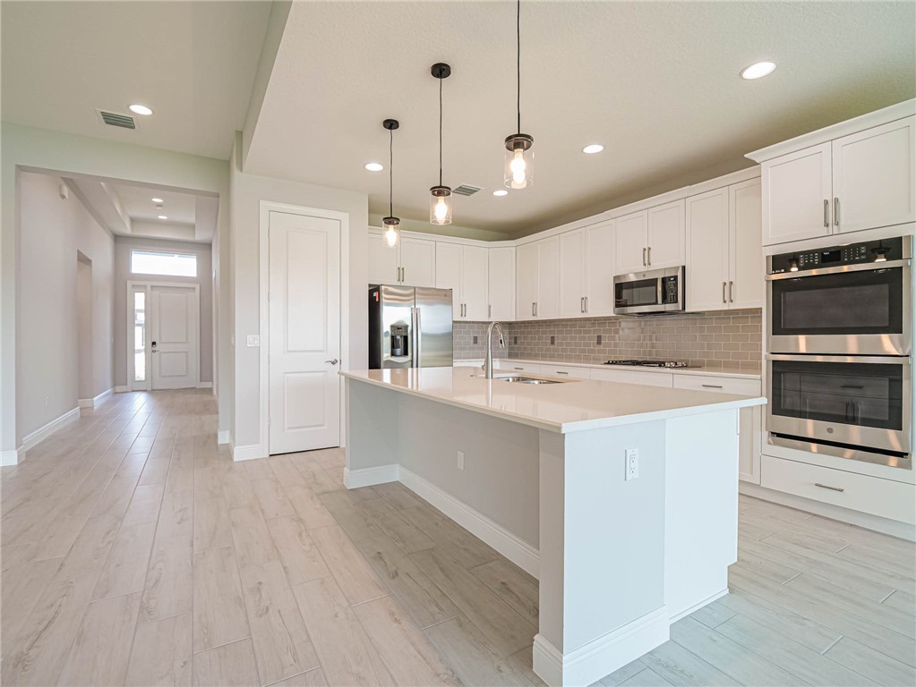6422 High Pointe W Way Vero Beach, FL 32967 - Photo 5 of 33 a large kitchen with kitchen island a stove a sink a refrigerator and a microwave oven with wooden floor