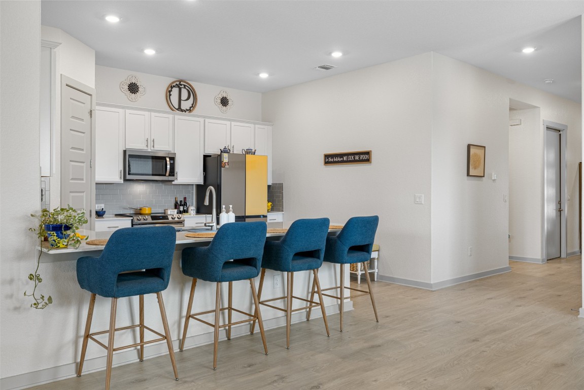 109 Rambling Rapids Drive Georgetown, TX 78628 - Photo 11 of 37 Kitchen featuring a kitchen bar, decorative backsplash, light wood finished floors, a peninsula, and white cabinetry