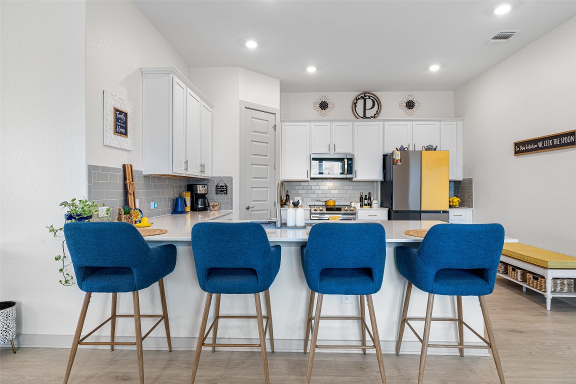 109 Rambling Rapids Drive Georgetown, TX 78628 - Photo 10 of 37 Kitchen with a peninsula, white cabinets, light wood-style floors, tasteful backsplash, and recessed lighting
