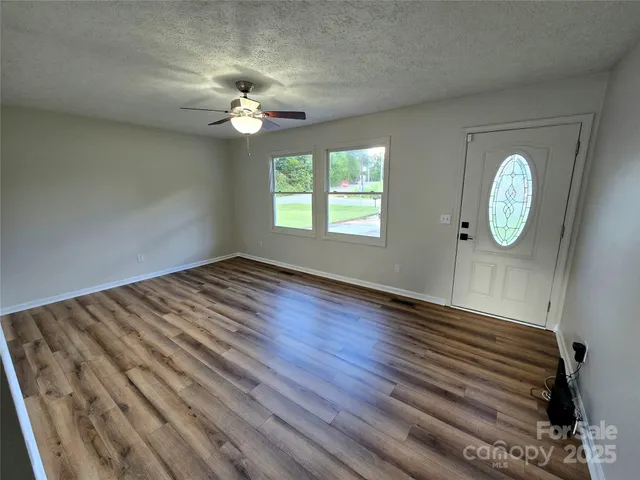 an empty room with wooden floor fan and windows