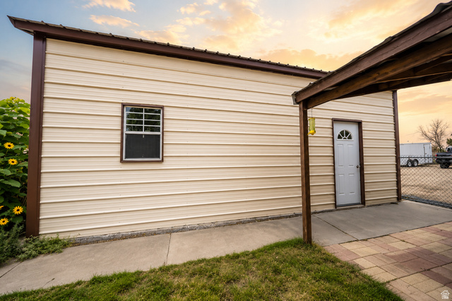 305 West Elmo Road Elmo, UT 84521 - Photo 23 of 27 Cream-colored metal siding with dark brown trim, a covered entryway, a white panel door with an arched window, and a concrete walkway leading to a paver patio