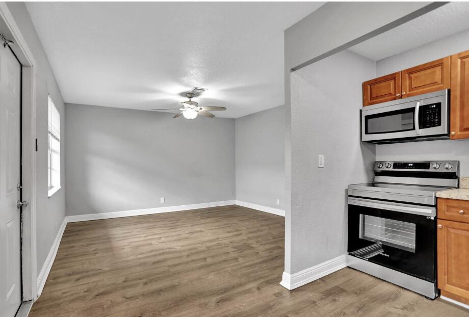 a view of an empty room with wooden floor and a kitchen
